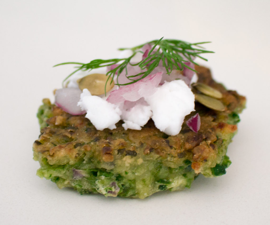 Closeup of a green pea fritter with vegan feta, red onion and dill