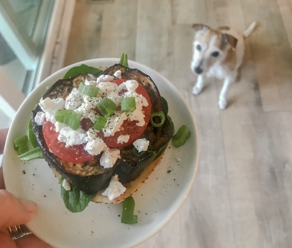 top bagel with eggplant and tomatoes with small dog in background