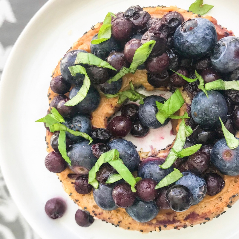top view bagel with almond butter, sauteed frozen blueberries, fresh blueberries, fresh basil