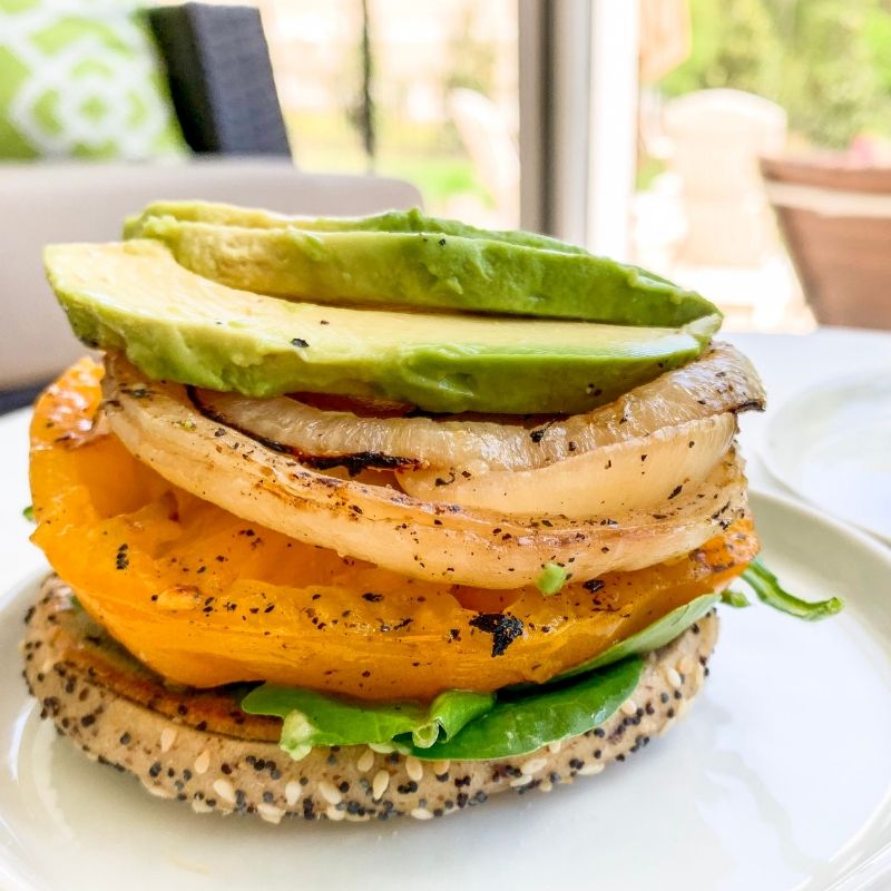 Side view bagel with grilled organic yellow tomato, grilled onions, sliced avocado, organic baby spinach