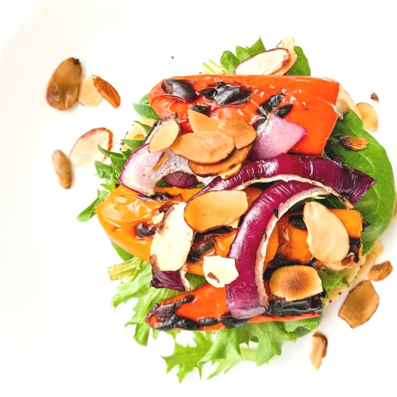 top view mixed greens, charred colorful peppers, red onions, roasted silvered almonds
